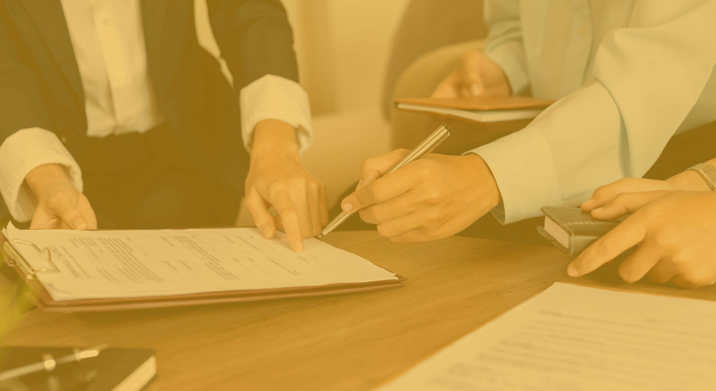 People's hands signing a document on a clipboard